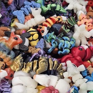 May include: A collection of colorful, 3D-printed figurines in various shapes, including animals and abstract forms. The figurines are in shades of orange, blue, white, yellow, and red. The image is a close-up, showing the details of the plastic toys.