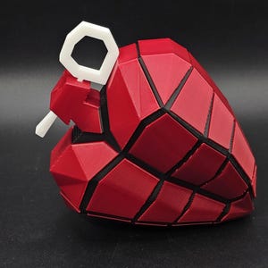 May include: A red and black heart-shaped grenade with a white pull ring. The grenade is made of a 3D printed material and has a geometric design.