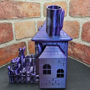 May include: A purple 3D printed haunted house with a fence, ghosts, and a chimney. The house has two windows and a brick pattern.