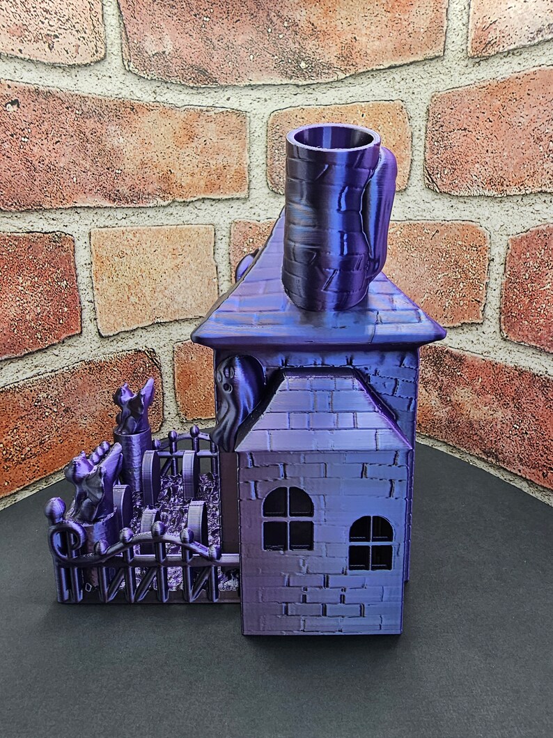 May include: A purple 3D printed haunted house with a fence, ghosts, and a chimney. The house has two windows and a brick pattern.