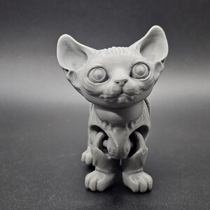 May include: A gray 3D printed figurine of a hairless cat with large eyes and a playful expression. The cat is standing on all fours and has a jointed body.