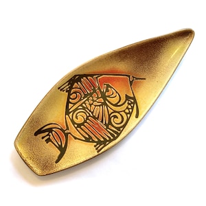 May include: An oblong decorative dish featuring a fish motif. The dish has a speckled gold and brown finish. The fish is rendered in black, orange, and red, with detailed patterns. The dish is likely made of ceramic or metal.