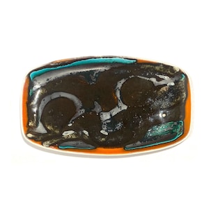 Op de afbeelding: Rechthoekige keramische schaal met een glanzend, abstract ontwerp. De schaal heeft een donkerbruin midden met witte, turquoise en groene accenten. De rand is omzoomd met oranje en wit. Een uniek stuk om te serveren of tentoon te stellen.