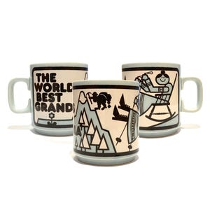 Könnte beinhalten: Drei hellblaue Keramikbecher mit schwarzen grafischen Illustrationen. Ein Becher zeigt den Text THE WORLD BEST GRANDS. Ein weiterer zeigt eine Person in einem Schaukelstuhl, und der dritte stellt eine Berglandschaft mit einer Figur dar.