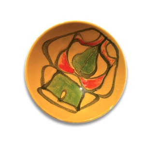 Op de afbeelding: Een gele keramische kom met een abstract ontwerp in groen, rood en zwart.