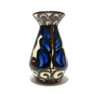 Peut inclure: Un vase en céramique avec un bord évasé et un corps fuselé, présentant une base de couleur crème décorée de motifs floraux bleu cobalt peints à la main et d'accents tourbillonnants brun foncé qui enveloppent toute la surface extérieure.