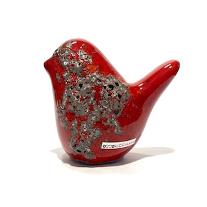 Peut inclure: Figurine d'oiseau en céramique rouge brillant avec une tache texturée grise sur le corps. L'oiseau a un petit bec et une queue incurvée. La figurine porte une étiquette "OTTOKERAMIK".