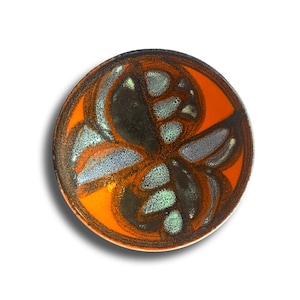 Könnte beinhalten: Ein runder Keramikteller mit orangefarbenem Zentrum und dunkelbraunem Rand. Der Teller hat ein stilisiertes Blumendesign in Schwarz, Grau und Türkis. Der Teller ist wahrscheinlich handgefertigt und eignet sich zum Servieren von Speisen oder als dekoratives Stück.