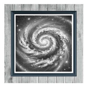 May include: Framed monochrome cross-stitch pattern of a spiral galaxy. The artwork is in a dark blue frame, set against a light grey wooden background. The text "SPIRAL GALAXY" and "MONOCHROME CROSS STITCH PATTERN" are displayed.