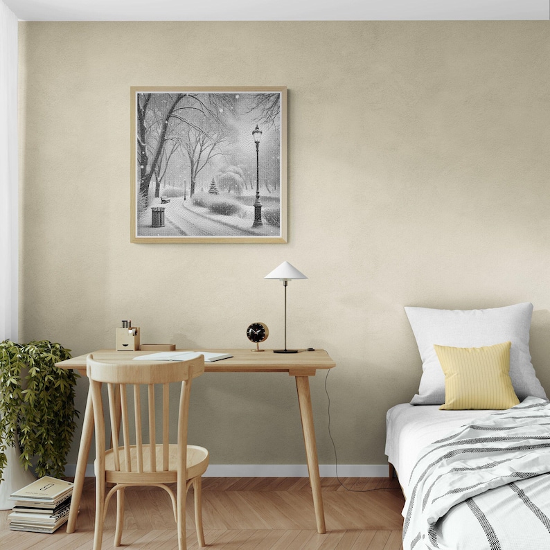May include: A black and white photograph of a snowy park scene with a lamppost in the centre. The photograph is framed in a light wood frame and is hanging on a beige wall.