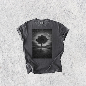 May include: Dark gray t-shirt featuring a black and white illustration of a tree with exposed roots on a hill, under a starry sky with a comet. The tee has rolled-up sleeves and a classic crew neck.