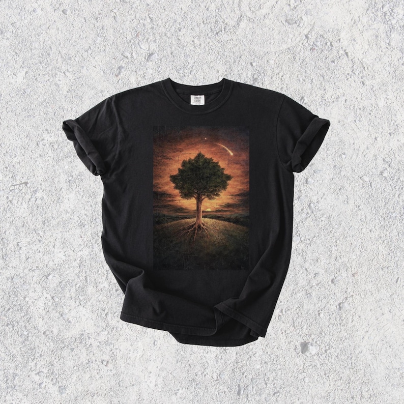 May include: Black t-shirt featuring a detailed illustration of a tree with exposed roots on a grassy hill, set against a sunset sky with a shooting star. The artwork is centered on the shirt.