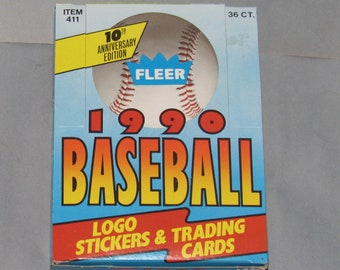 Può includere: Una scatola di carte da baseball Fleer del 1990. La scatola è blu e rossa con una palla da baseball bianca e il logo Fleer. La scatola dice "10th Anniversary Edition" e "36 CT."