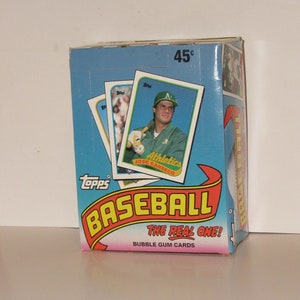 May include: A blue and red box with the words "Topps Baseball The Real One! Bubble Gum Cards" on the front. The box features a baseball card of Jose Canseco, an Oakland Athletics player, with the text "Athletics Jose Canseco" on the card. The box is priced at 45 cents.