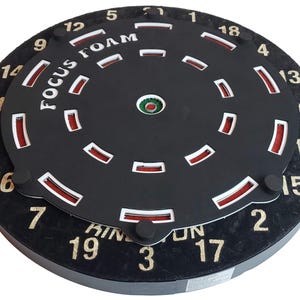 May include: A black dartboard with a red and white foam target insert. The target has numbers 1 through 19 around the outer edge. The text "FOCUS FOAM" is printed on the target.