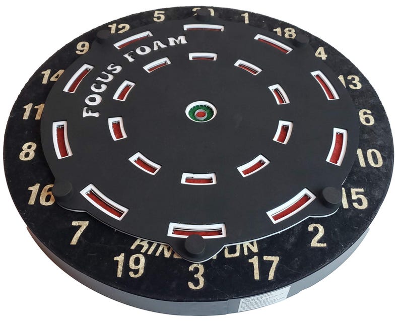 May include: A black dartboard with a red and white foam target insert. The target has numbers 1 through 19 around the outer edge. The text "FOCUS FOAM" is printed on the target.