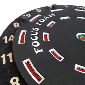 May include: A black circular object with the words "Focus Foam" printed in white. The object has a series of red and white markings around the edge. The numbers 1, 2, 5, 9, 11, 12, 14, and 8 are visible around the edge.