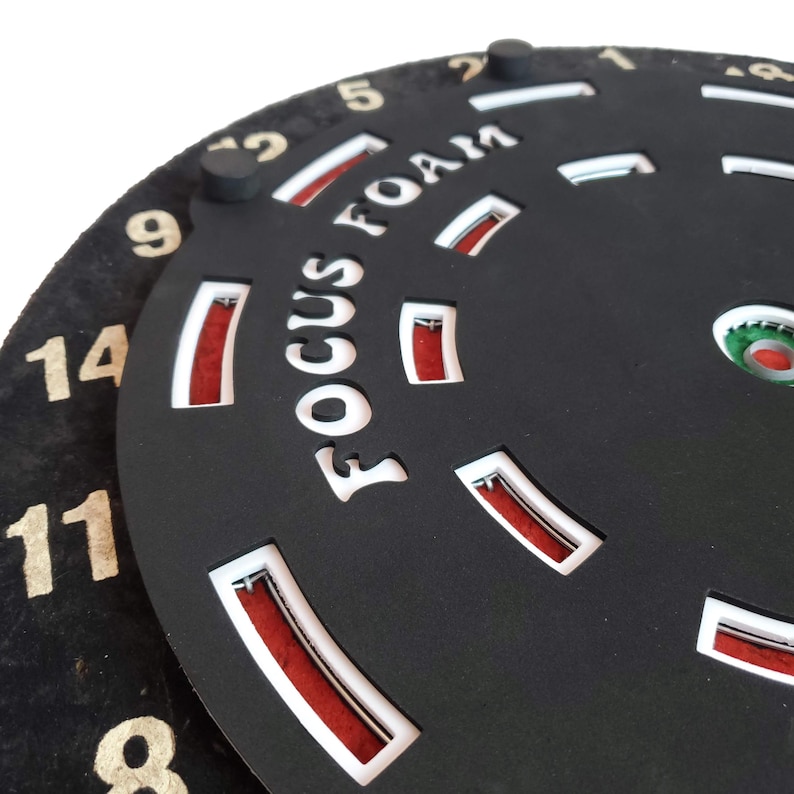May include: A black circular object with the words "Focus Foam" printed in white. The object has a series of red and white markings around the edge. The numbers 1, 2, 5, 9, 11, 12, 14, and 8 are visible around the edge.