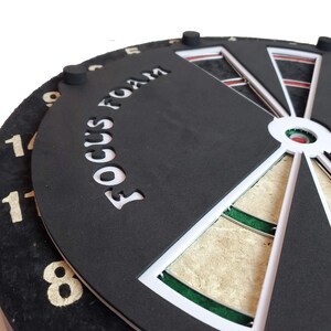 May include: A black dartboard with a white border and a white "Focus Foam" logo. The dartboard has a green and white bullseye and a red center.