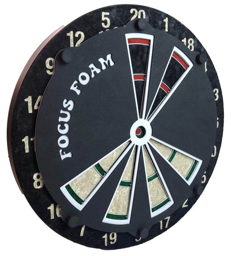 May include: A black dartboard with a white bullseye and green and white segments. The board has the words "FOCUS FOAM" printed on it in white letters. The numbers 1 through 20 are printed around the edge of the board in white.