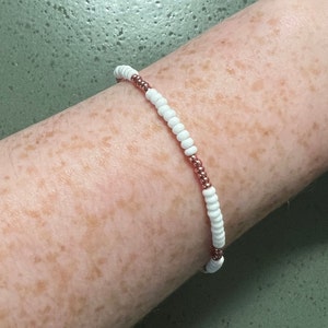 Puede incluir: Un brazalete de cuentas blancas y doradas en la muñeca de una persona.