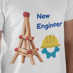 Puede incluir: Camiseta blanca con un gráfico de una torre de cerillas, un casco amarillo y un engranaje azul, con las palabras "New Engineer" en azul. La persona de la imagen lleva un casco blanco.