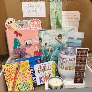 May include: A gift box filled with books, a tumbler, a candle, and stationery. The box includes a book with a woman in a blue dress, a pink notebook, and a tumbler that says "Don't talk to me, I'm reading!"