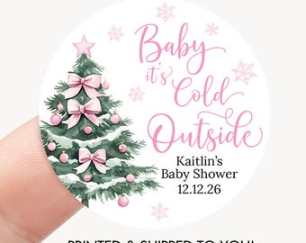 May include: A round sticker with a watercolor Christmas tree decorated with pink bows and ornaments. The text "Baby it's Cold Outside" is in pink script, with the name "Kaitlin's Baby Shower" and the date 12.12.26 below. The words "PRINTED & SHIPPED TO YOU!" are at the bottom.