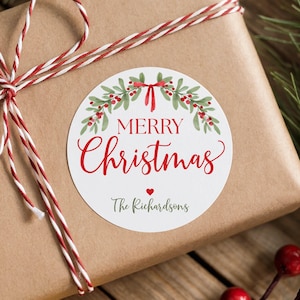 May include: A round white sticker featuring a watercolor illustration of green holly leaves and red berries arranged in a wreath shape. The text reads Merry Christmas in red, with The Richardsons printed below a small red heart.