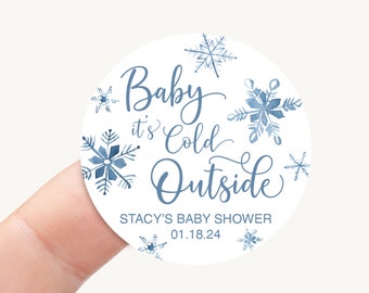 May include: Round white sticker with blue watercolor snowflakes and the text "Baby it's Cold Outside" in blue cursive font. The text "Stacy's Baby Shower 01.18.24" is also included in blue font.