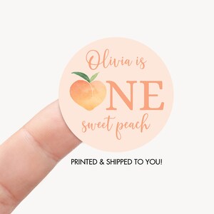 May include: Peach-themed first birthday party sticker with the text "Olivia is one sweet peach".