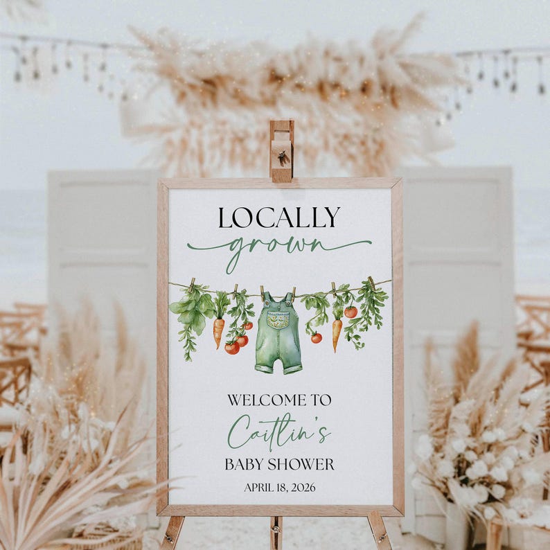 May include: A wooden framed sign with the words "Locally Grown" in a script font. Below is a watercolor illustration of vegetables and overalls hanging on a clothesline. The sign welcomes guests to "Caitlin's Baby Shower" on April 18, 2026.