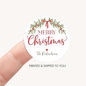May include: A round white sticker featuring a watercolor illustration of green holly leaves and red berries arranged in a wreath with a red bow at the top. The text reads Merry Christmas in red script and print, followed by a small red heart and The Richardsons.
