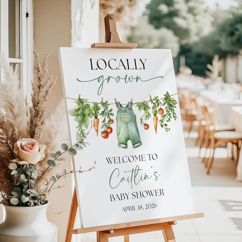 May include: A white sign on a wooden easel with the text "Locally Grown" and "Welcome to Caitlin's Baby Shower April 18, 2026." The sign features a watercolor illustration of vegetables and overalls.