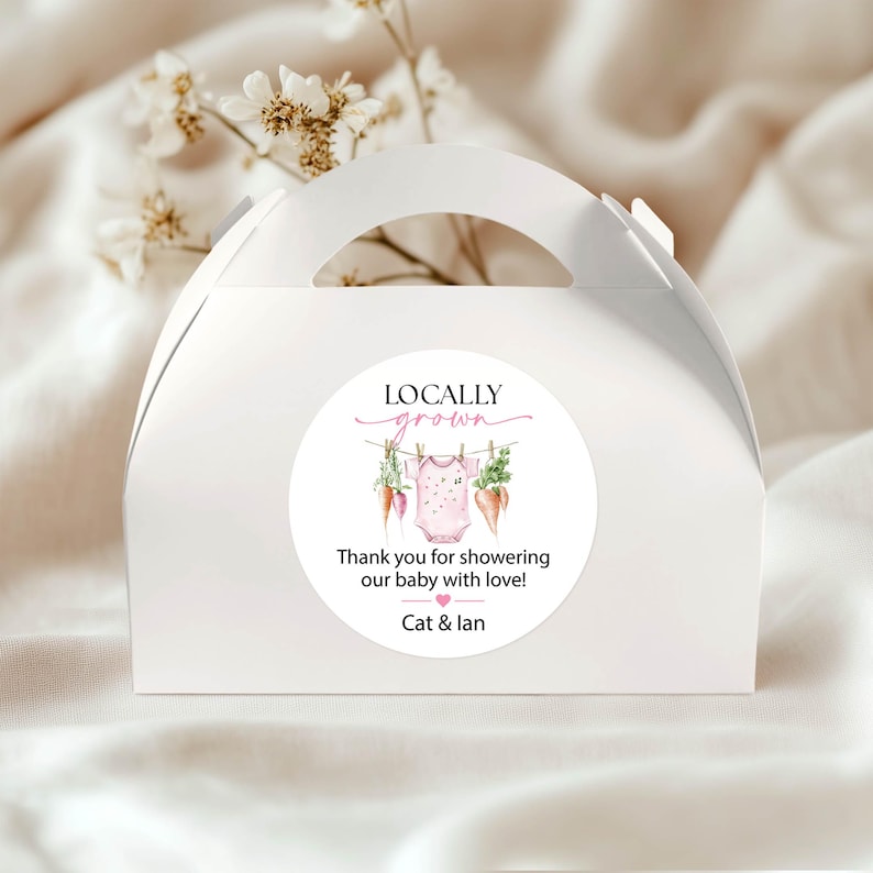 May include: White gable box with a round sticker. The sticker reads "Locally Grown" above a baby onesie, carrots, and greenery. The text "Thank you for showering our baby with love!" and the names "Cat & Ian" are also on the sticker.