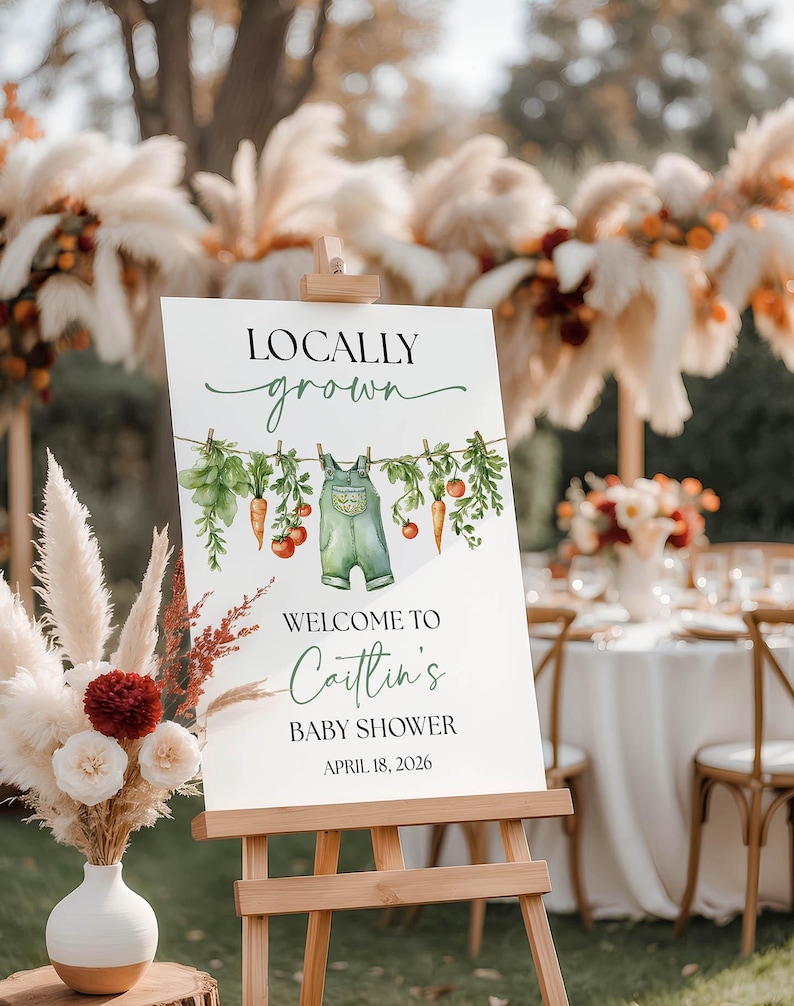 May include: A white sign on a wooden easel with the text "Locally Grown" and "Welcome to Caitlin's Baby Shower April 18, 2026." The sign features watercolor illustrations of vegetables and overalls.