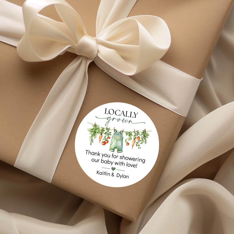 May include: A gift wrapped in brown paper with a cream-colored ribbon and bow. A round sticker on the package reads "Locally Grown" with a watercolor illustration of baby overalls and vegetables. The text says, "Thank you for showering our baby with love!" and the names Kaitlyn & Dylan.