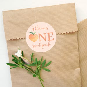 May include: A peach-colored circle sticker with a peach illustration and the text "Olivia is ONE sweet peach".