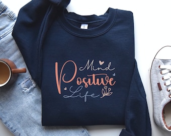 May include: Navy blue sweatshirt with the text "Mind Positive Life" in pink and gray lettering with small hearts and floral accents.