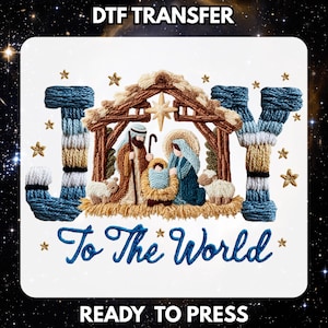 May include: A DTF transfer featuring the word JOY with a nativity scene inside the letter O, and the text To The World below. The design includes a stable, figures of Mary, Joseph, and baby Jesus, sheep, and gold stars on a white background.