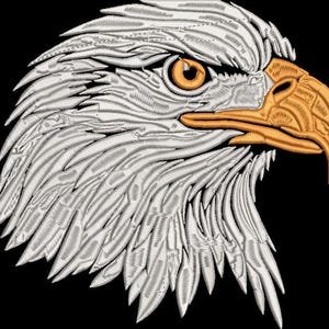 Puede incluir: Imagen bordada de la cabeza de un águila de perfil sobre un fondo negro. El águila presenta plumas blancas, un pico dorado y un ojo naranja. El bordado detallado da una apariencia texturizada.