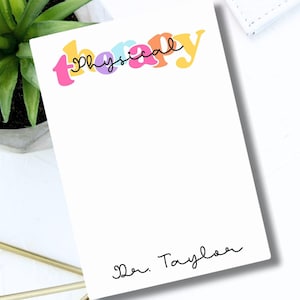 May include: A white notepad with the text "physical therapy" in colorful letters and the name "Dr. Taylor" written in black ink at the bottom.