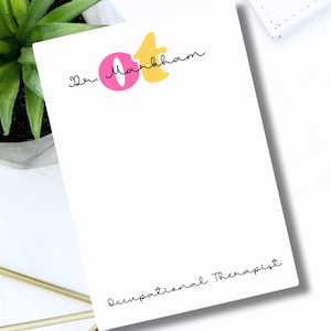 May include: White notepad with a pink and yellow logo that says "Jen Markham OT" and the text "Occupational Therapist" at the bottom.