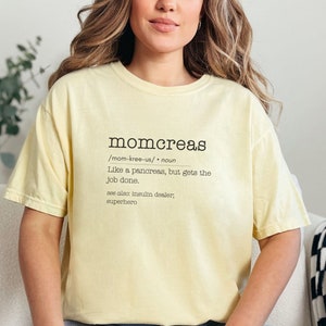 May include: A yellow t-shirt with a definition of the word "momcreas" printed on it. The definition reads: "Like a pancreas, but gets the job done. See also: insulin dealer, superhero."