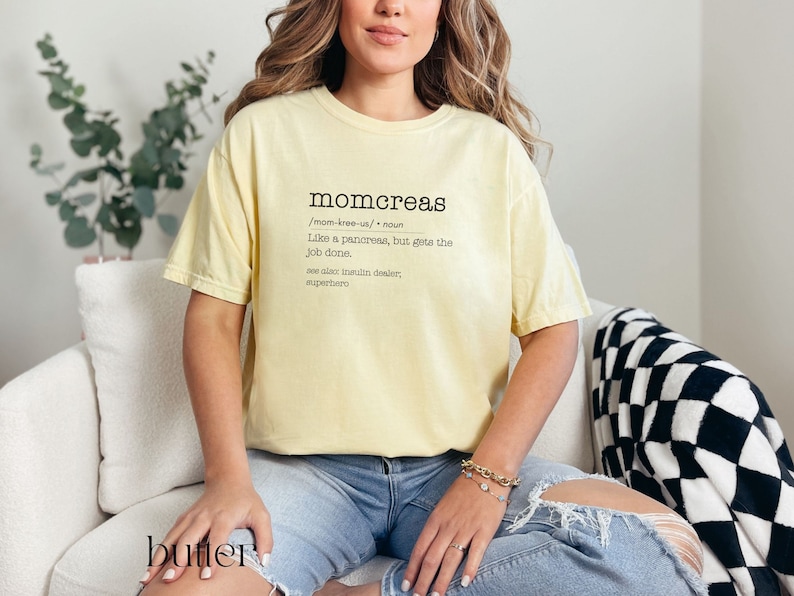 May include: A yellow t-shirt with a definition of the word "momcreas" printed on it. The definition reads: "Like a pancreas, but gets the job done. See also: insulin dealer, superhero."