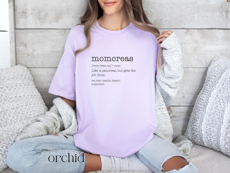 May include: A lavender t-shirt with the text "momcreas /mom-kree-us/ noun Like a pancreas, but gets the job done. see also insulin dealer, superhero" printed on the front.