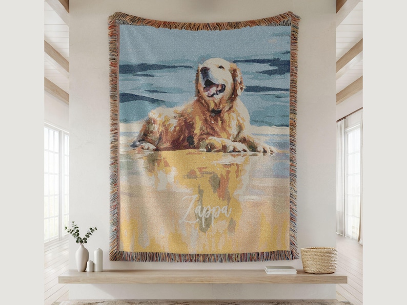 May include: Woven throw blanket featuring a golden retriever dog lying on a beach. The dog is depicted in shades of gold, brown, and white, with a blue and yellow background. The name "Zappa" is written on the blanket.