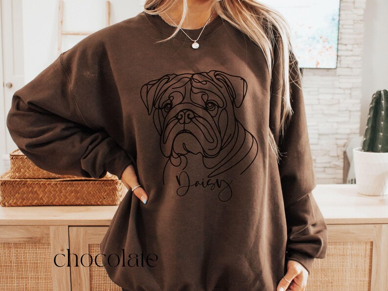 K&ouml;nnte beinhalten: Schokoladenfarbenes Sweatshirt mit einer Strichzeichnung eines Bulldoggen-Gesichts. Das Wort "Daisy" ist in Kursivschrift unter dem Bild des Hundes geschrieben. Das Wort "chocolate" ist unten auf dem Sweatshirt aufgedruckt.