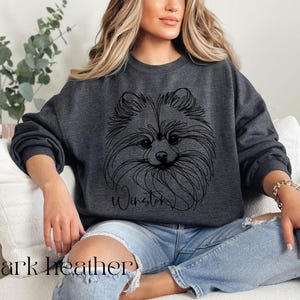 May include: Dark heather gray sweatshirt featuring a line drawing of a Pomeranian dog's face. The dog's name, "Winston", is written below the image in a script font. The words "dark heather" are printed at the bottom of the image.