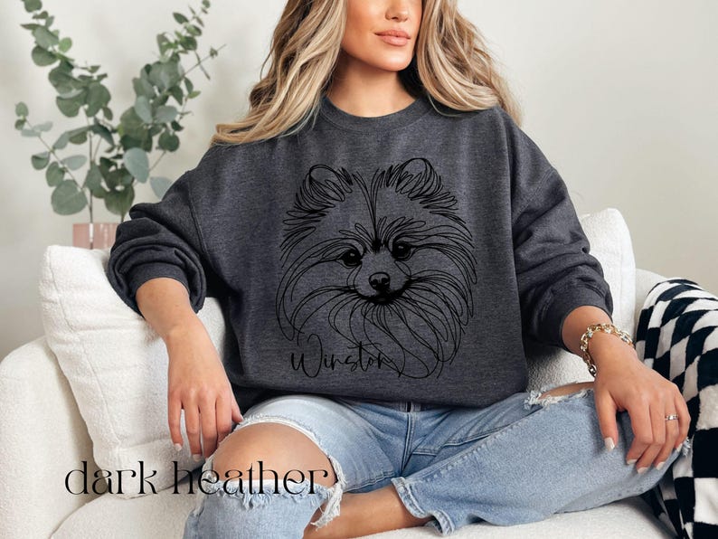 May include: Dark heather gray sweatshirt featuring a line drawing of a Pomeranian dog's face. The dog's name, "Winston", is written below the image in a script font. The words "dark heather" are printed at the bottom of the image.